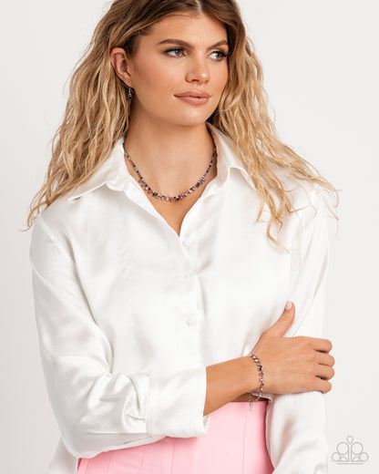 Woman wearing a white blouse with a necklace and pink pants on a light background