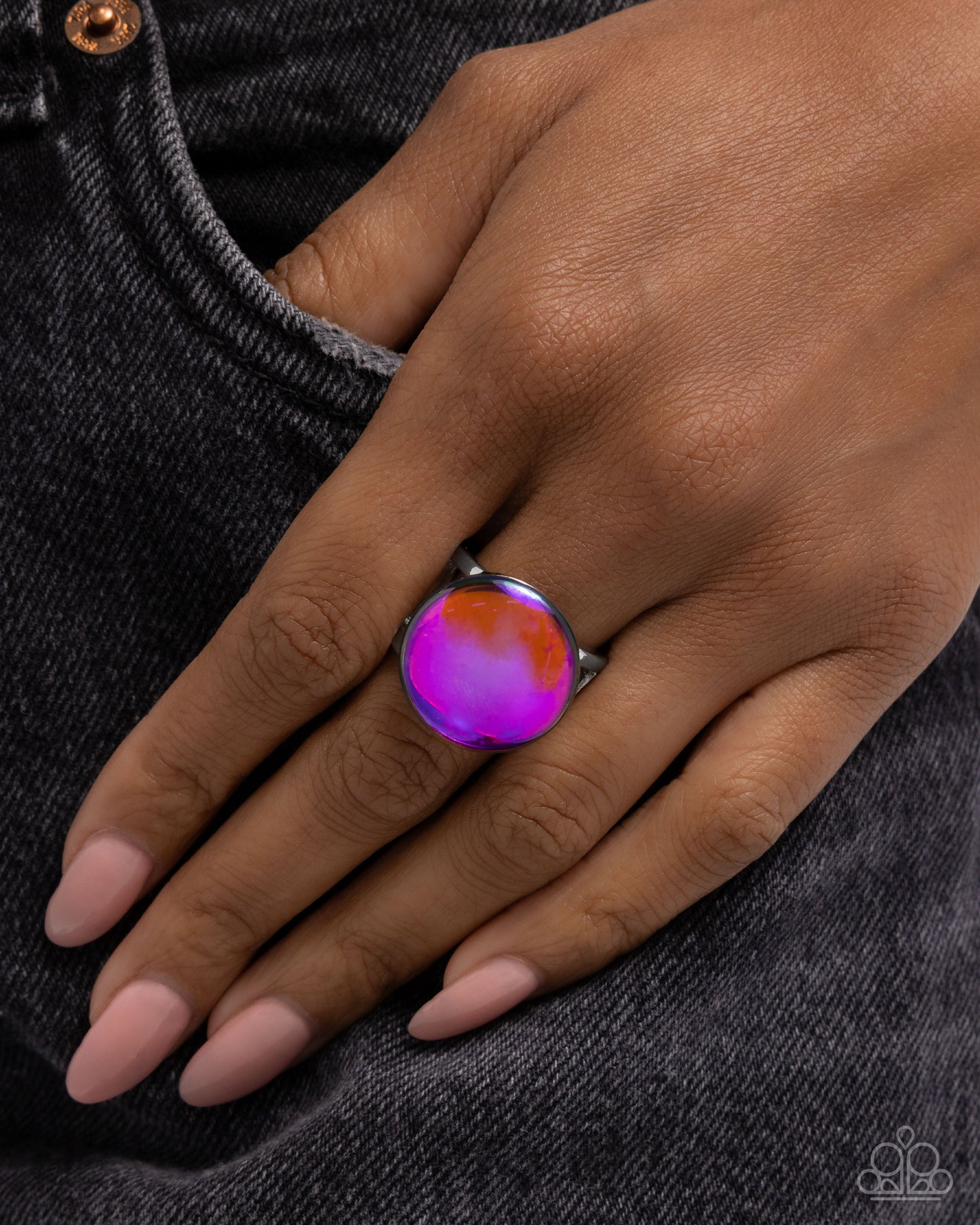 Hand wearing a colorful ring on a dark denim background