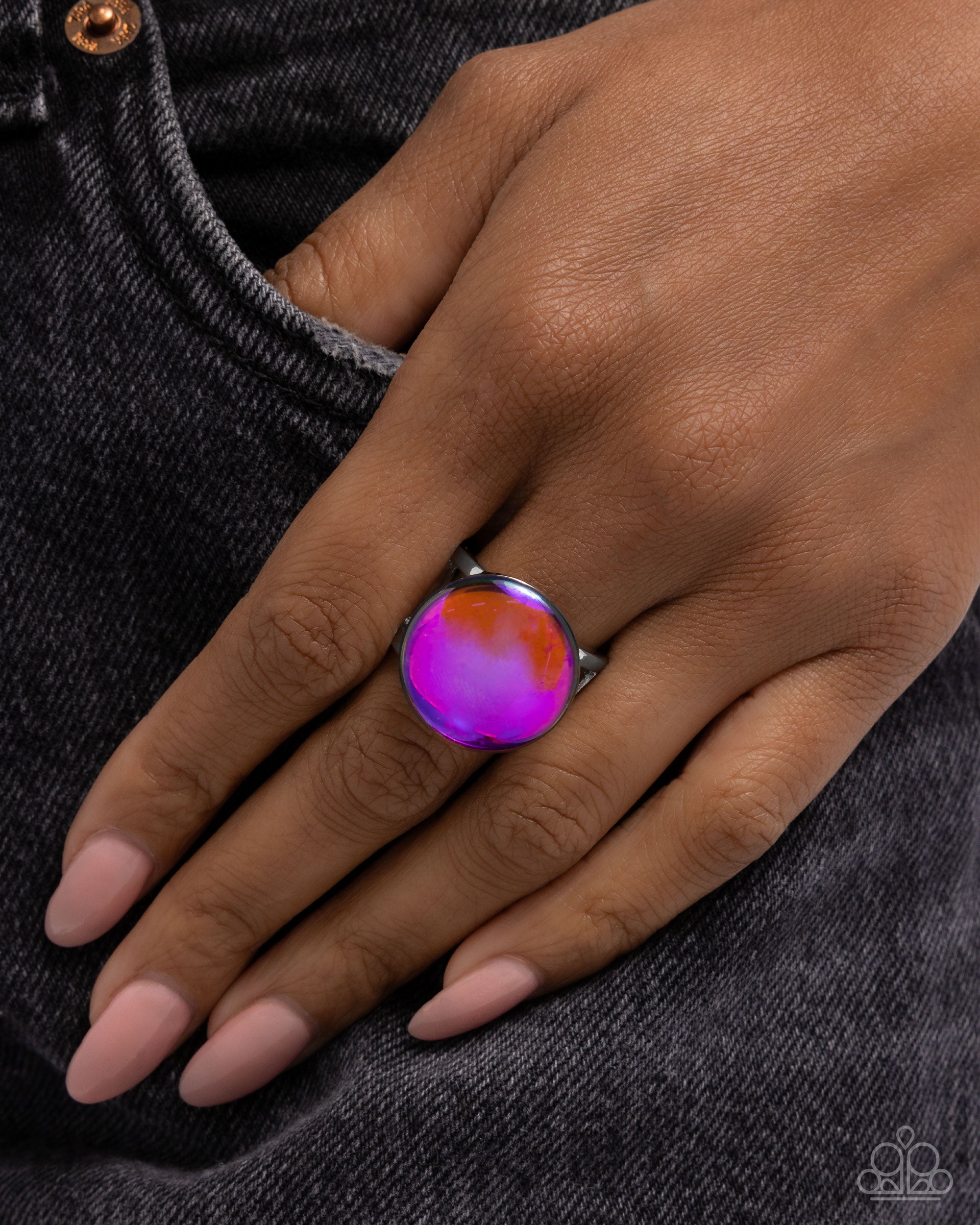 Hand wearing a colorful ring on a dark denim background