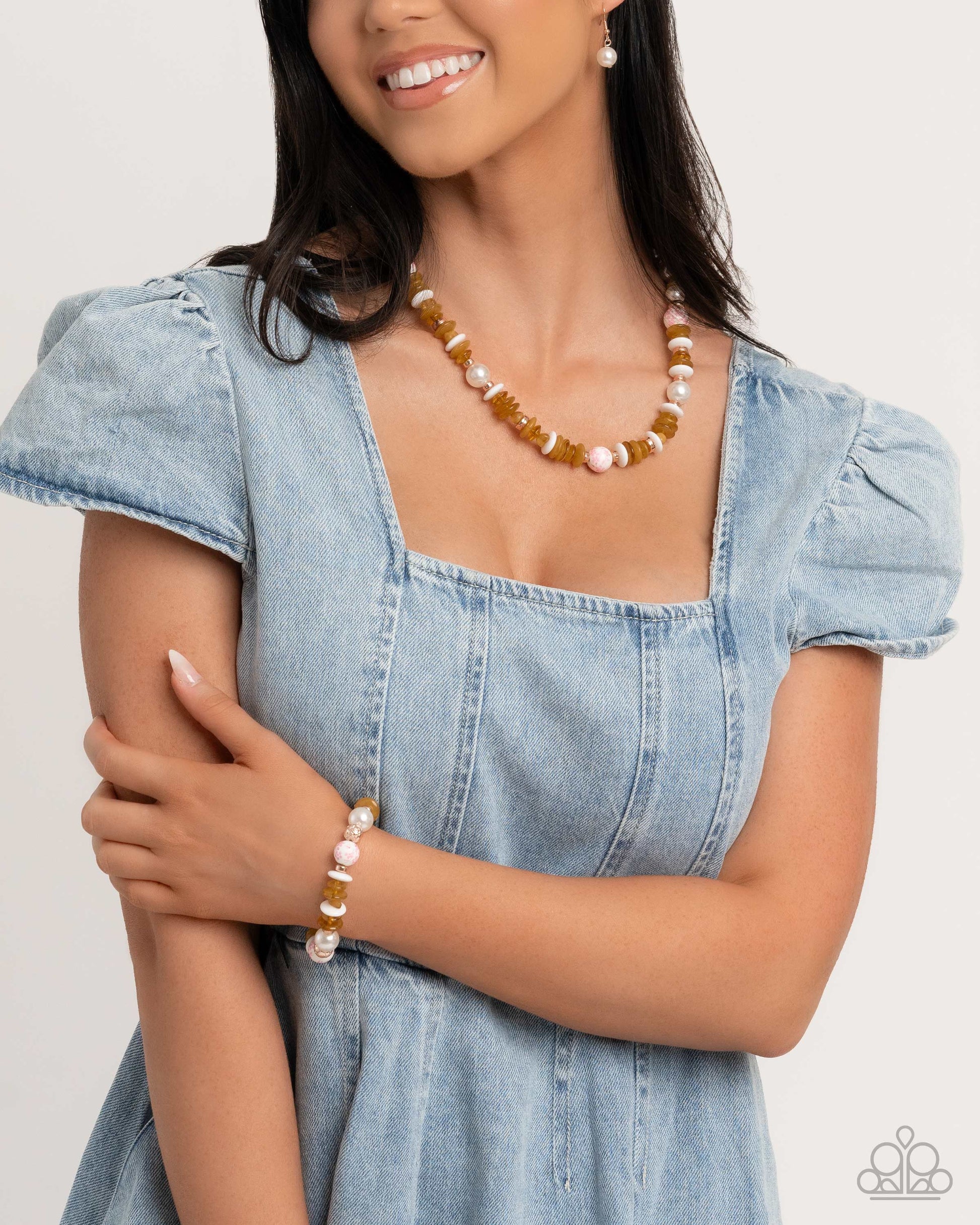 A woman wearing a denim dress and a beaded necklace with a mix of white pearls, rose gold beads, and golden palm beads.