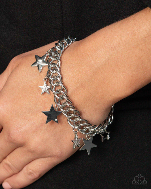 Silver chain bracelet with star charms on a wrist against a black background