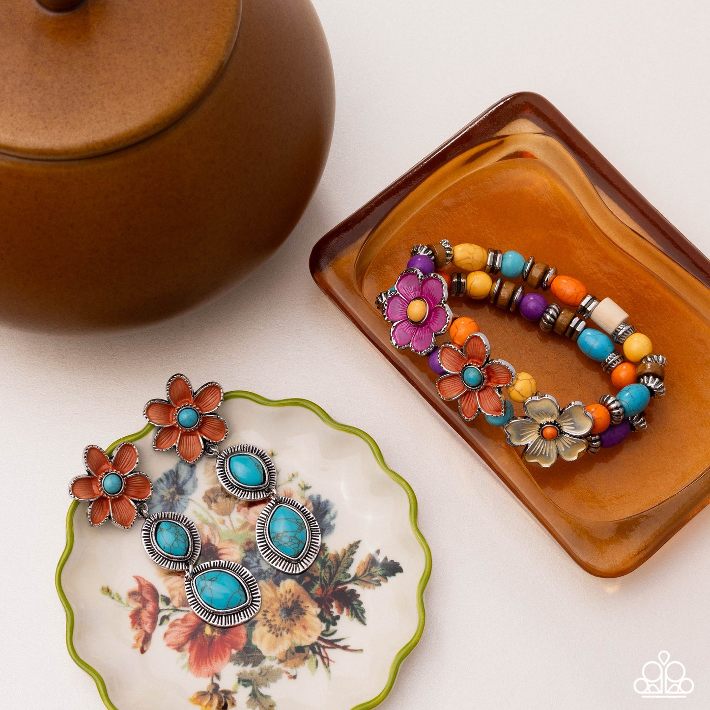 Pair of floral earrings on a decorative plate with a colorful beaded bracelet on a matching tray.