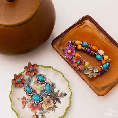 Pair of floral earrings on a decorative plate with a colorful beaded bracelet on a matching tray.