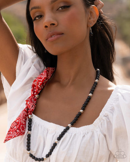 Woman wearing a white top with a red bandana and a black beaded necklace outdoors