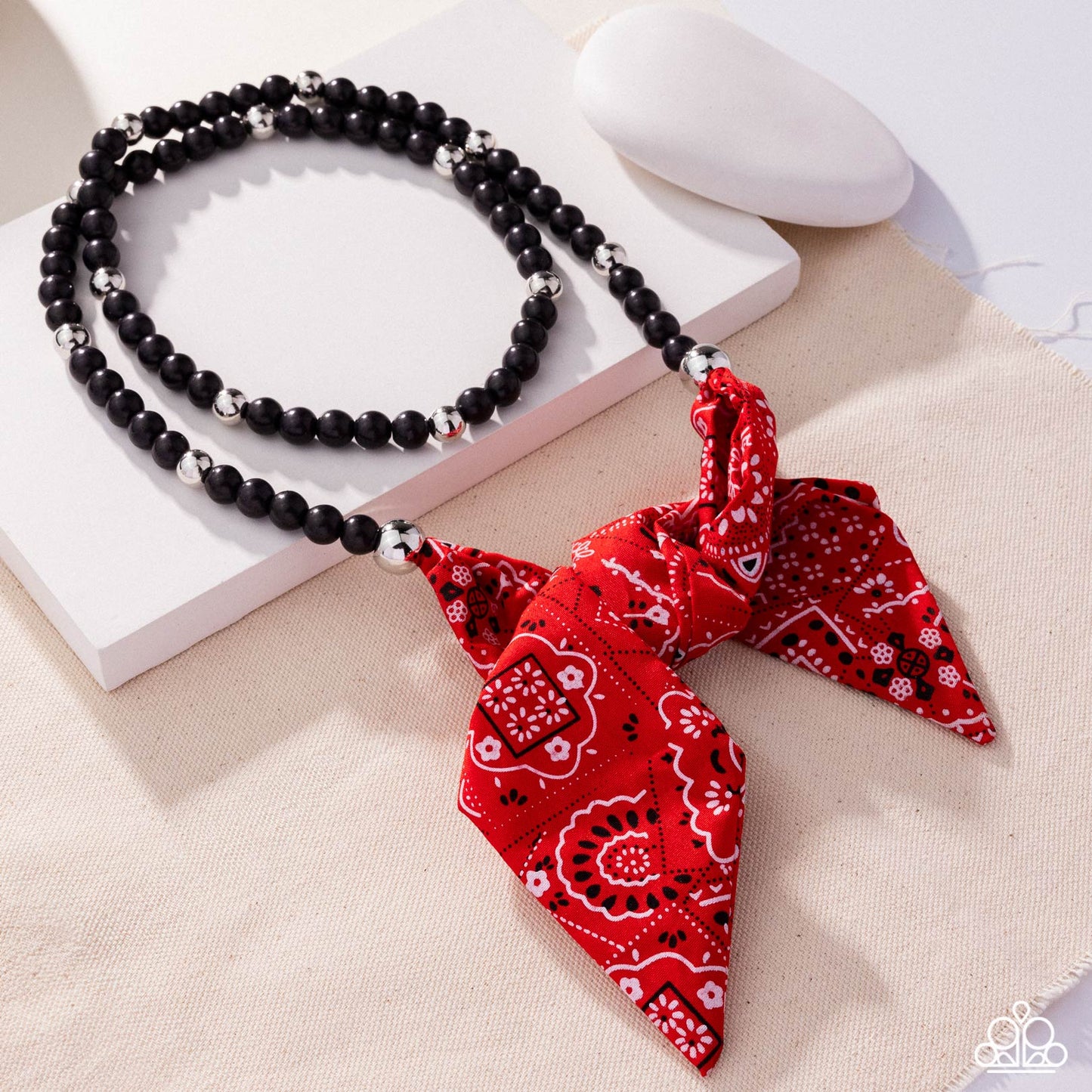 Necklace with black beads and a red bandana pendant on a white surface