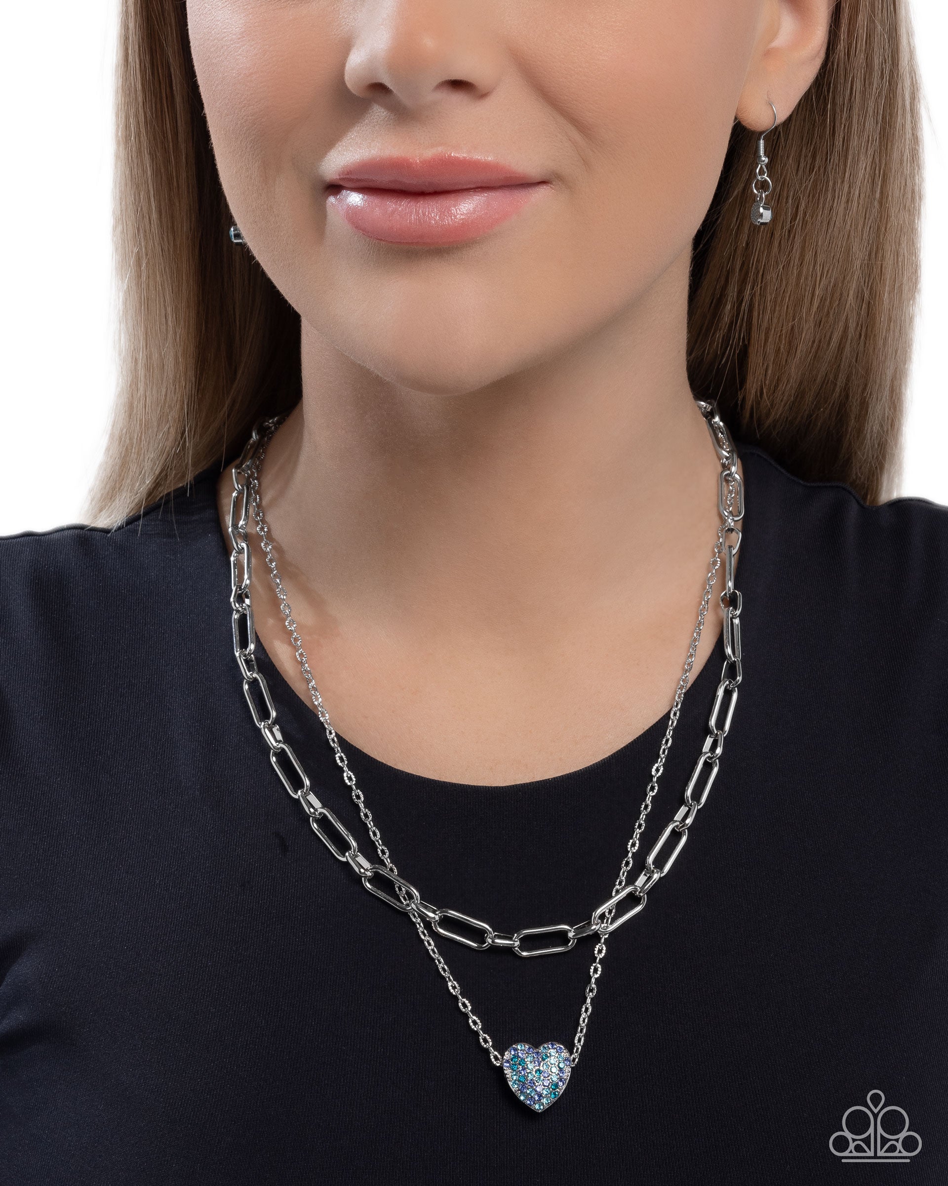 Woman wearing a silver chain necklace with a heart pendant on a plain background