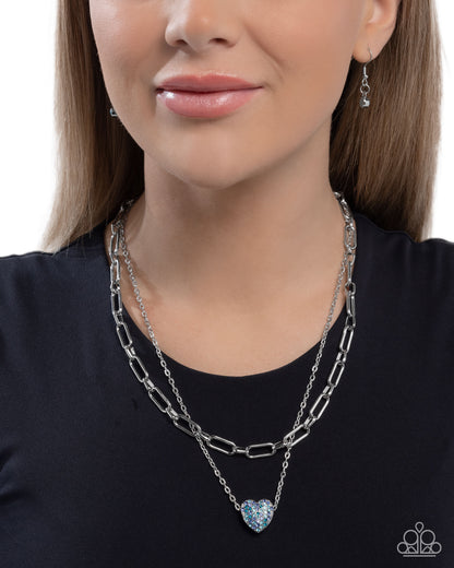Woman wearing a silver chain necklace with a heart pendant on a plain background