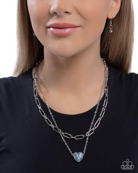 Woman wearing a silver chain necklace with a heart pendant on a plain background