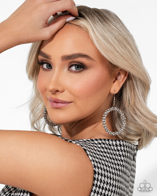 Woman with styled hair and large hoop earrings against a neutral background