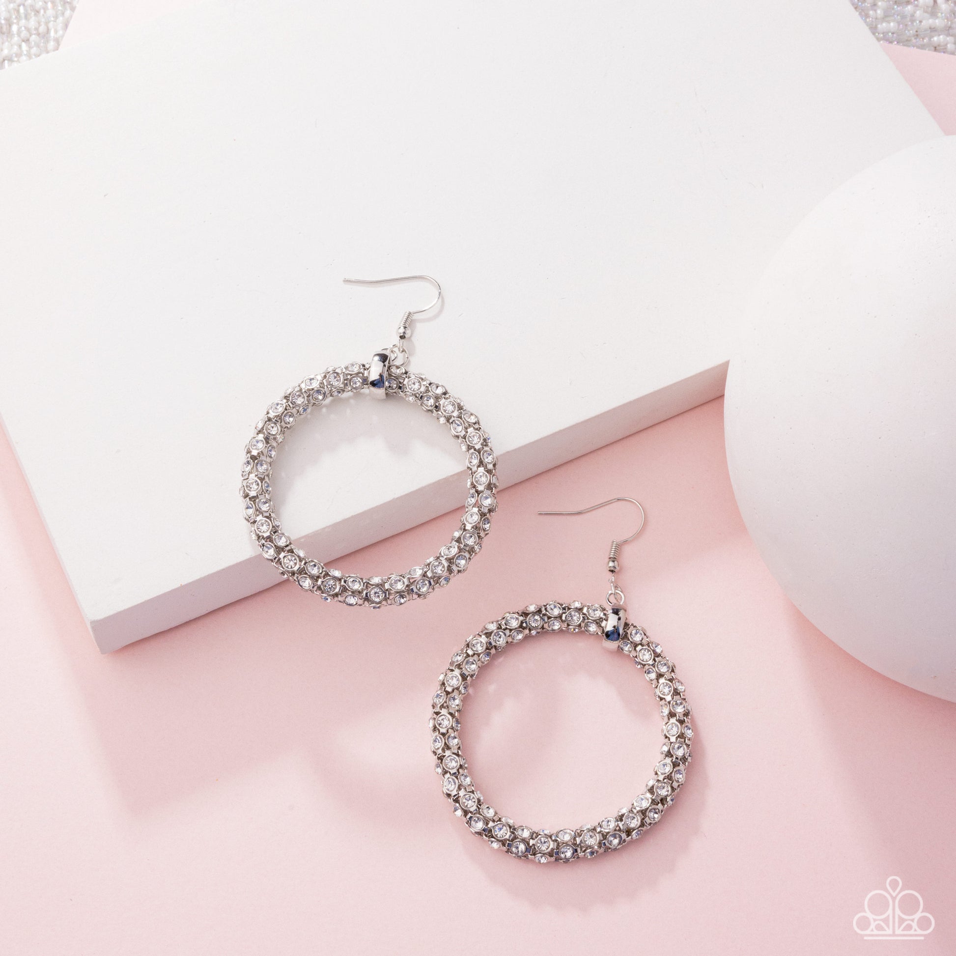 Silver hoop earrings with rhinestones on a pink surface