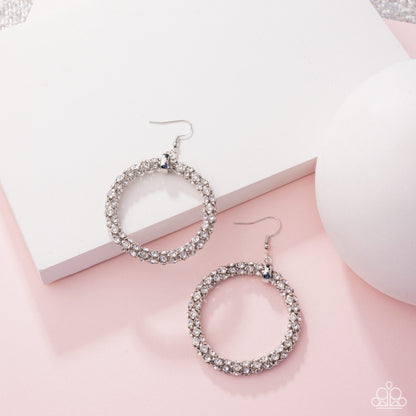 Silver hoop earrings with rhinestones on a pink surface