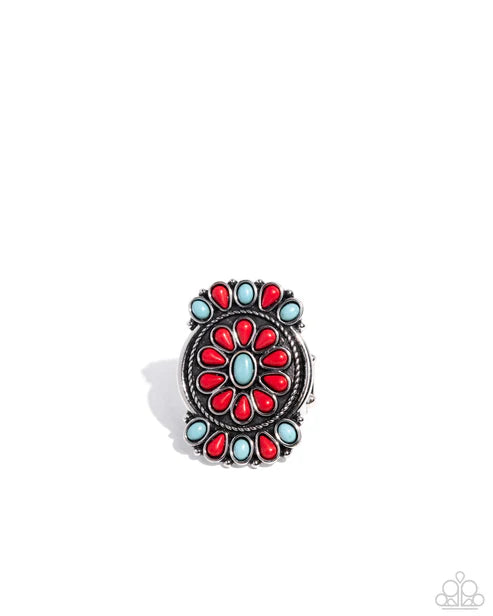 A Southwestern-style silver ring featuring a central oval motif with red teardrop stones and light blue oval stones, surrounded by a border of light blue and red stones, shown on a white background.