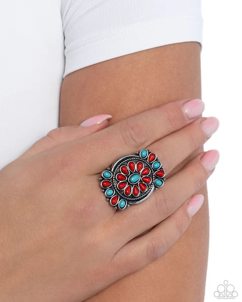 Close-up of a hand wearing a colorful ring with turquoise and red stones on a white background