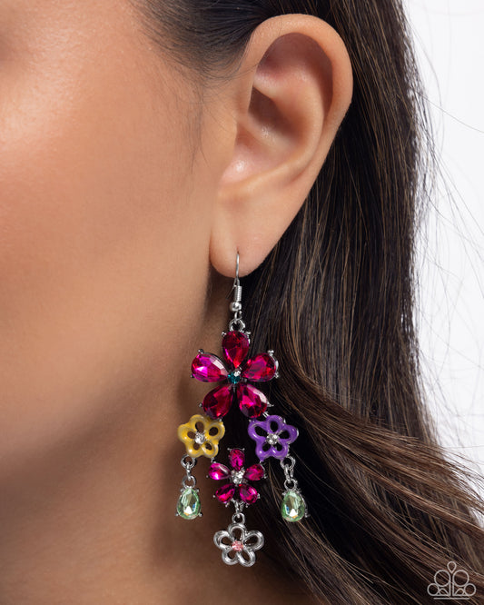 Close-up of an ear wearing a colorful flower-shaped earring with dangling charms.