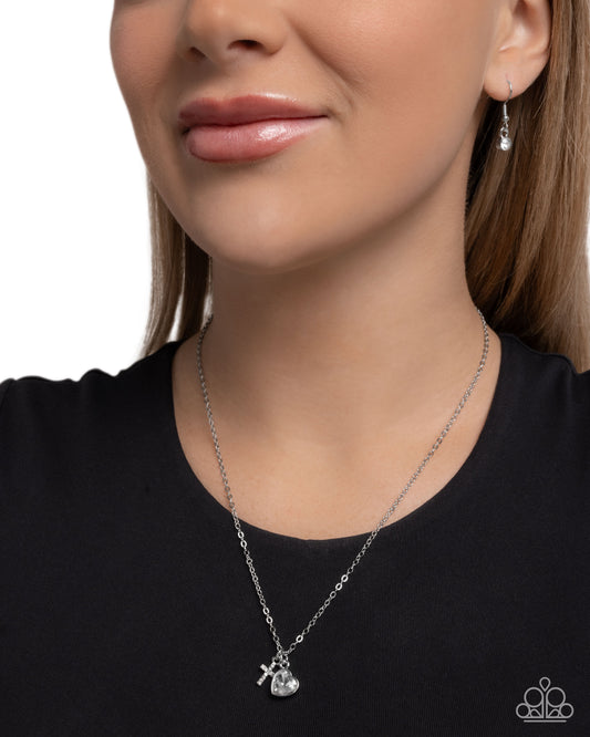 Close-up of a woman wearing a silver necklace with a heart pendant on a plain background