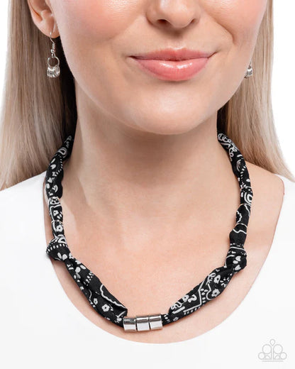 Woman wearing a black and white patterned necklace with matching earrings on a white background