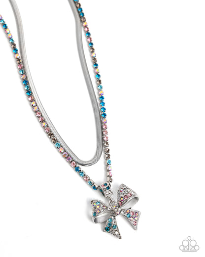 A silver-tone double-strand necklace featuring a snake chain and a beaded chain with a bow-shaped pendant, embellished with iridescent and pastel rhinestones, shown on a white background.