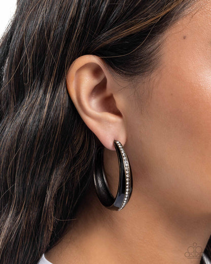 Black hoop earring with clear stones worn by a person with dark hair.
