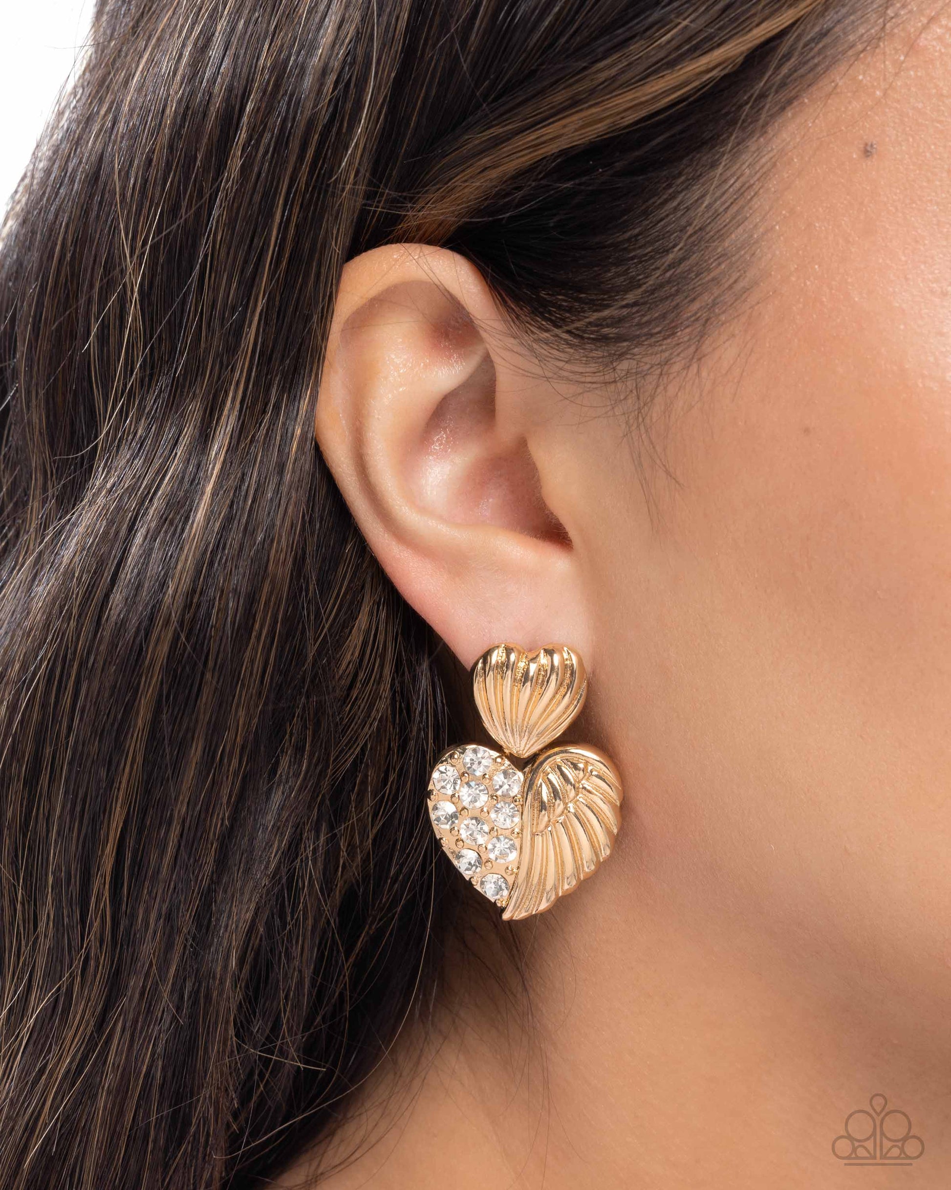 Gold heart-shaped earrings worn by a person with dark hair.