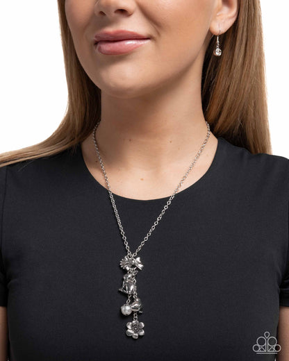 Woman wearing a silver necklace with floral pendants on a plain background