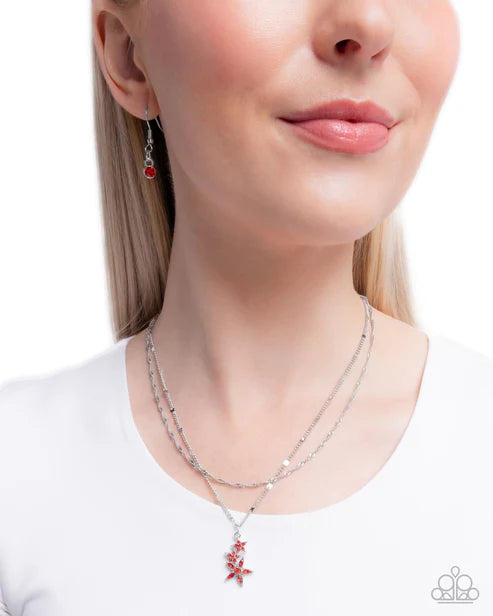 Close-up of a woman wearing a silver necklace with a red pendant and matching earrings on a white background.