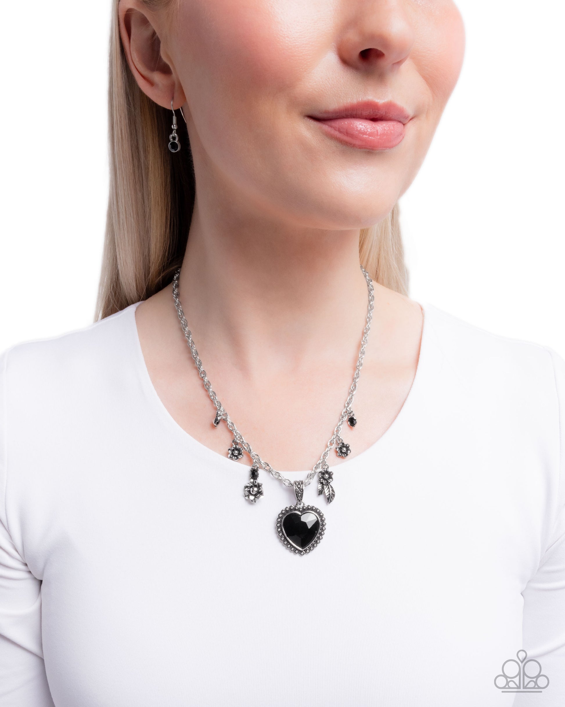 Woman wearing a silver necklace with a black heart pendant on a white background
