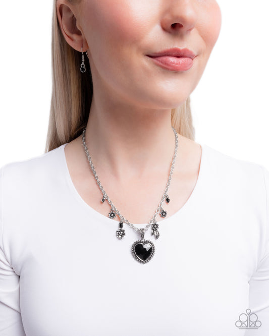 Woman wearing a silver necklace with a black heart pendant on a white background
