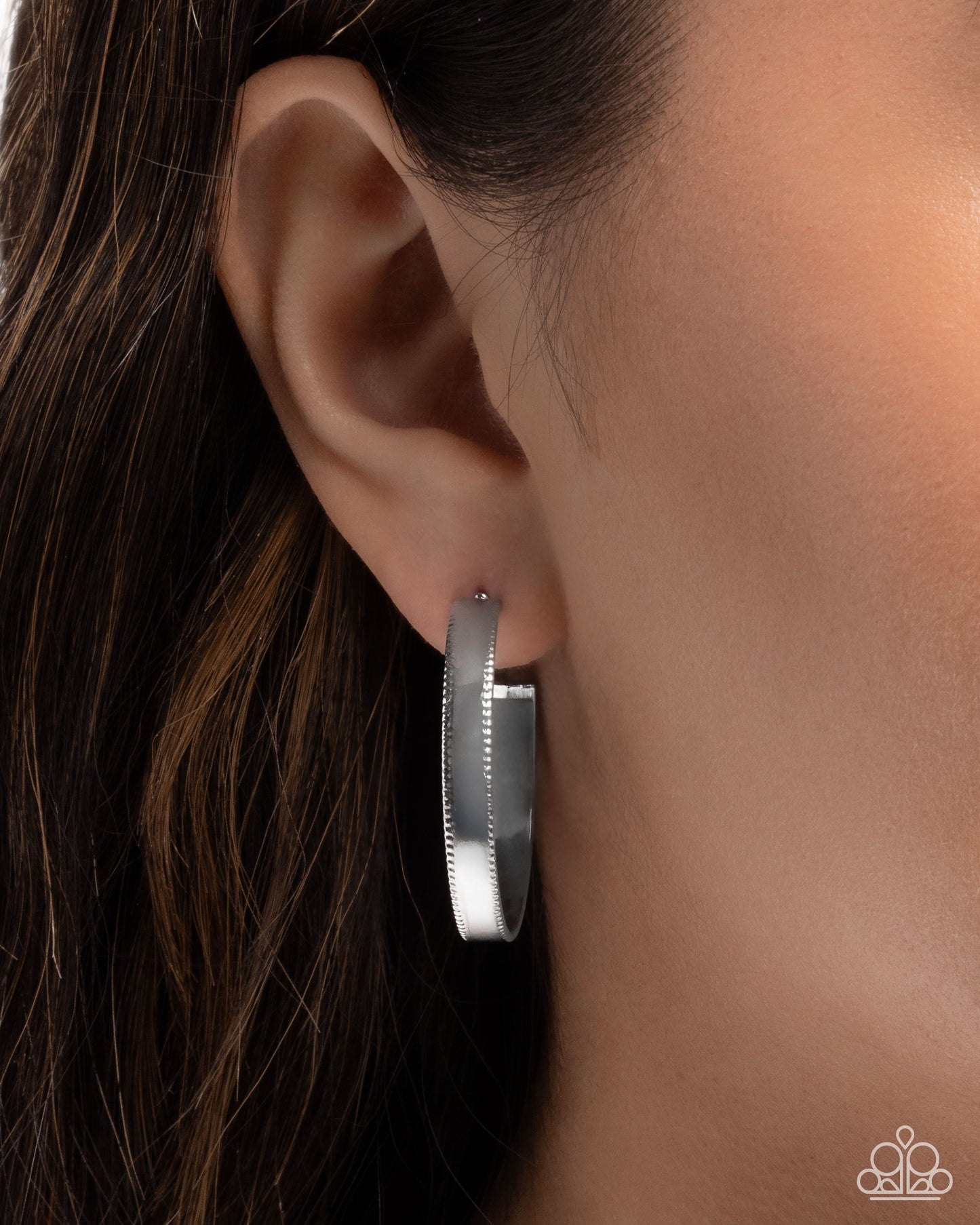 Silver hoop earring worn by a person with dark hair.