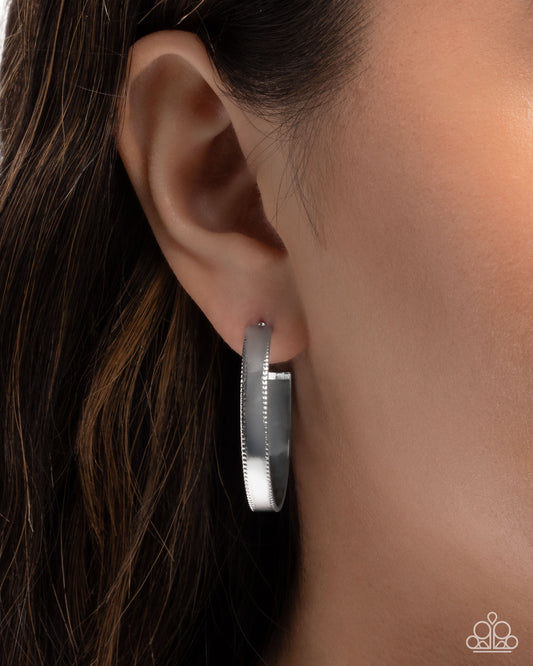Silver hoop earring worn by a person with dark hair.