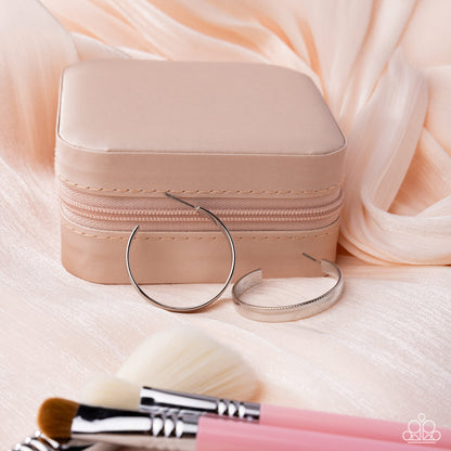 Small beige jewelry box with silver hoop earrings and makeup brushes on a soft pink fabric background