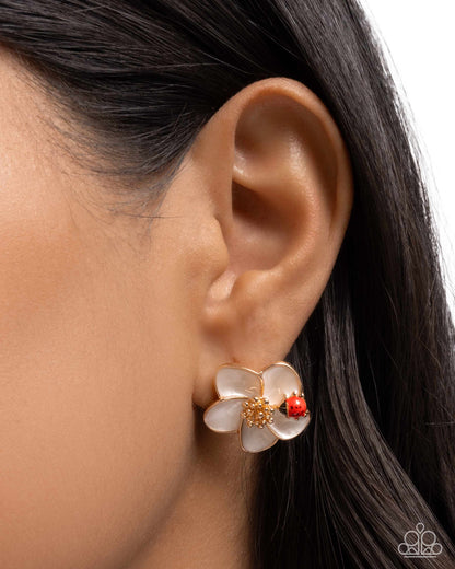 Close-up of an ear wearing a floral earring with red and gold accents.