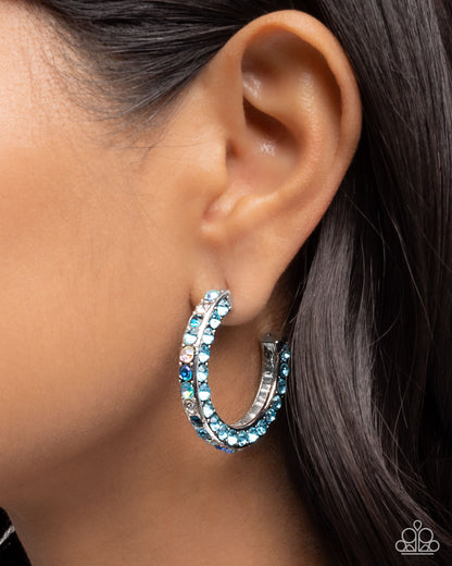 Close-up of an ear wearing a blue rhinestone hoop earring.