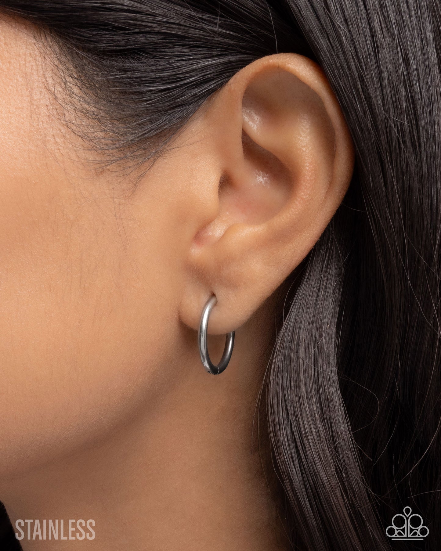 Close-up of an ear wearing a silver hoop earring with 'Stainless' text.