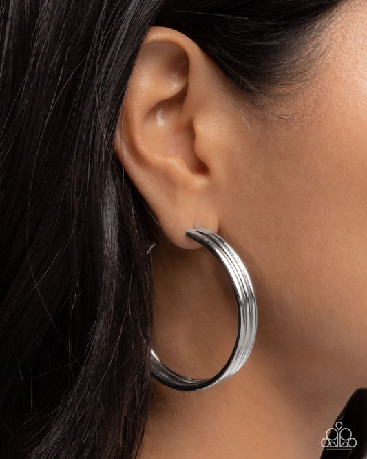 Silver hoop earring worn by a person with dark hair.