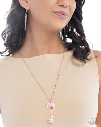 Woman wearing a rose gold necklace with a heart-shaped key pendant on a white background