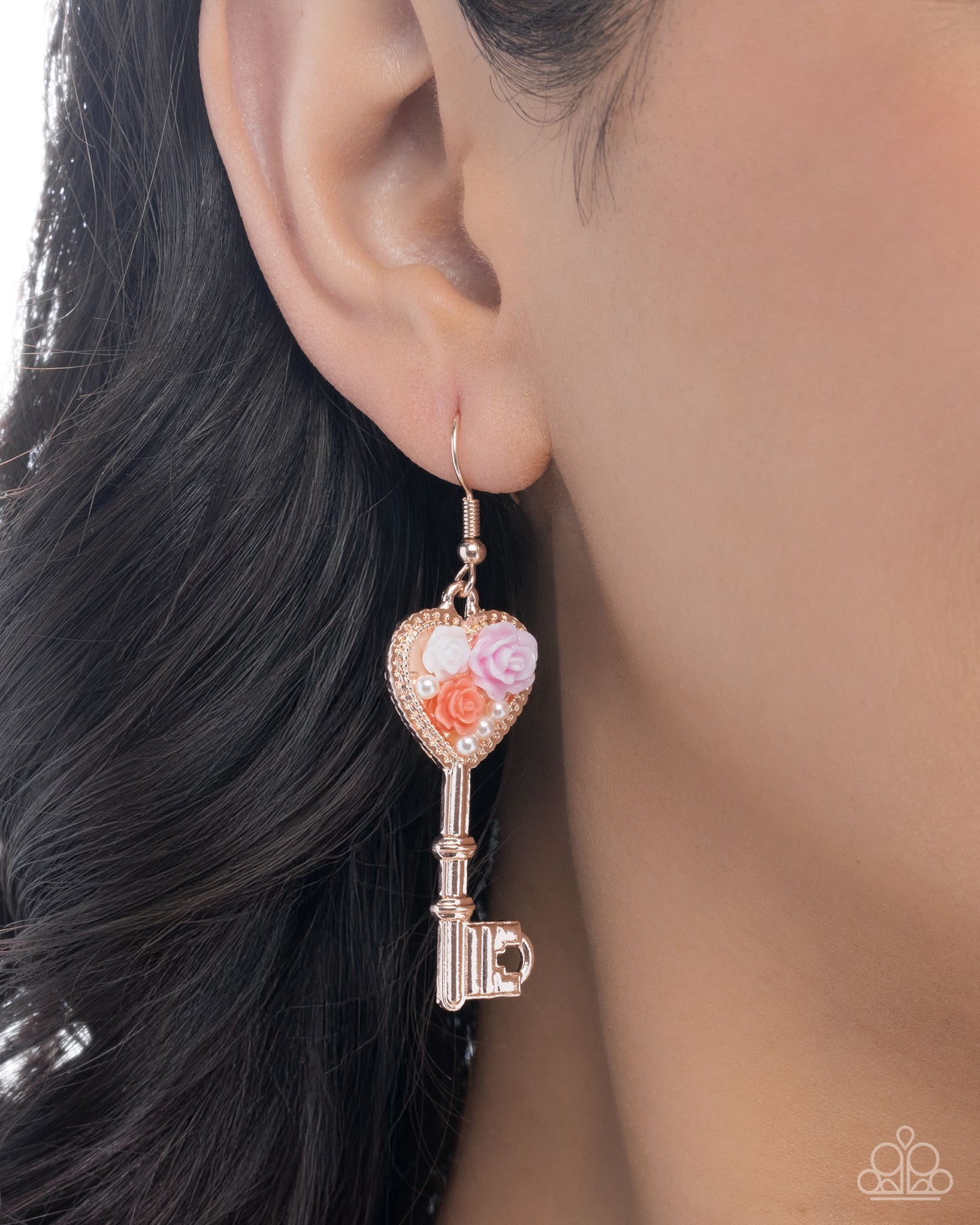 Close-up of an ear wearing a decorative key-shaped earring with floral elements.