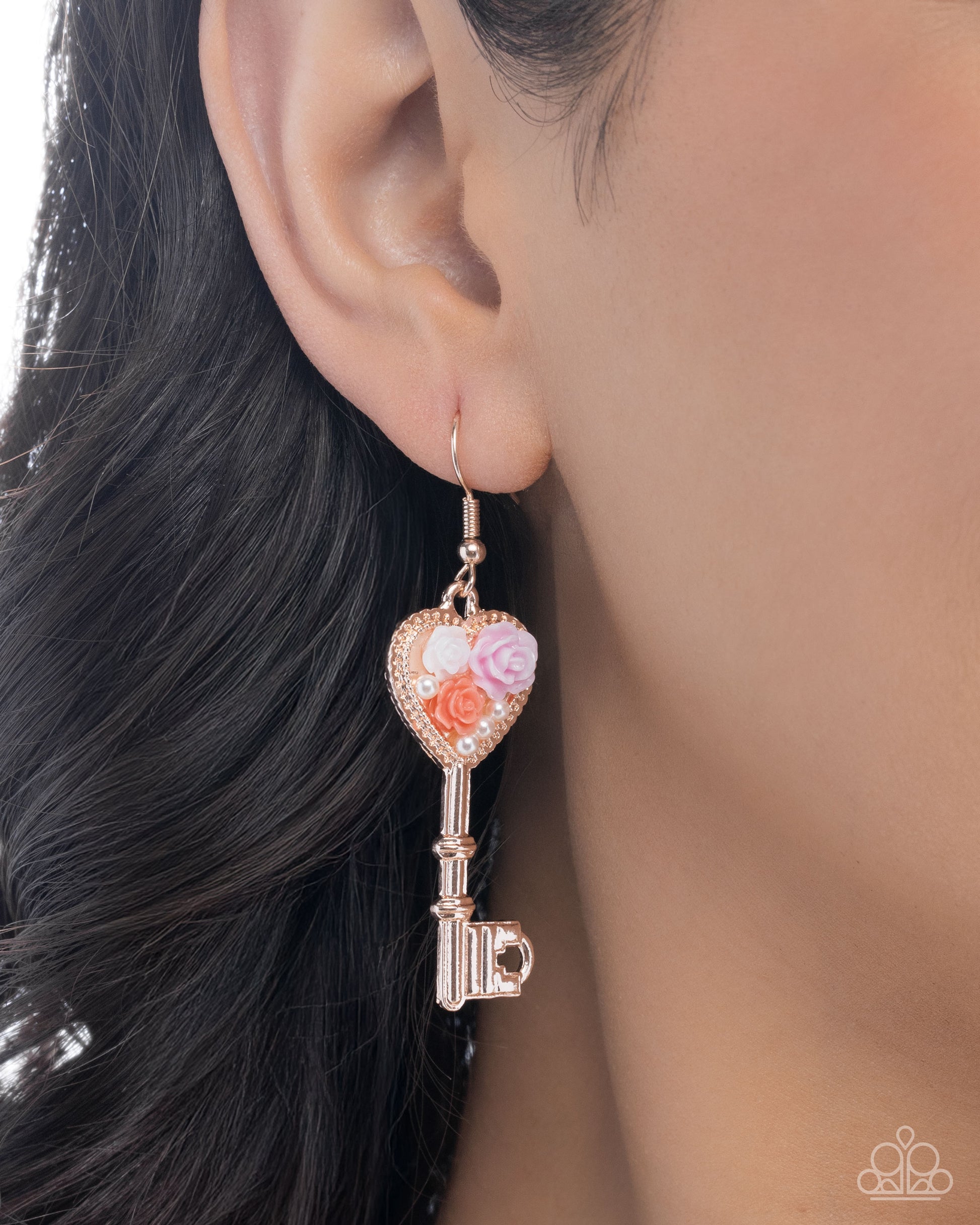 Close-up of an ear wearing a decorative key-shaped earring with floral elements.