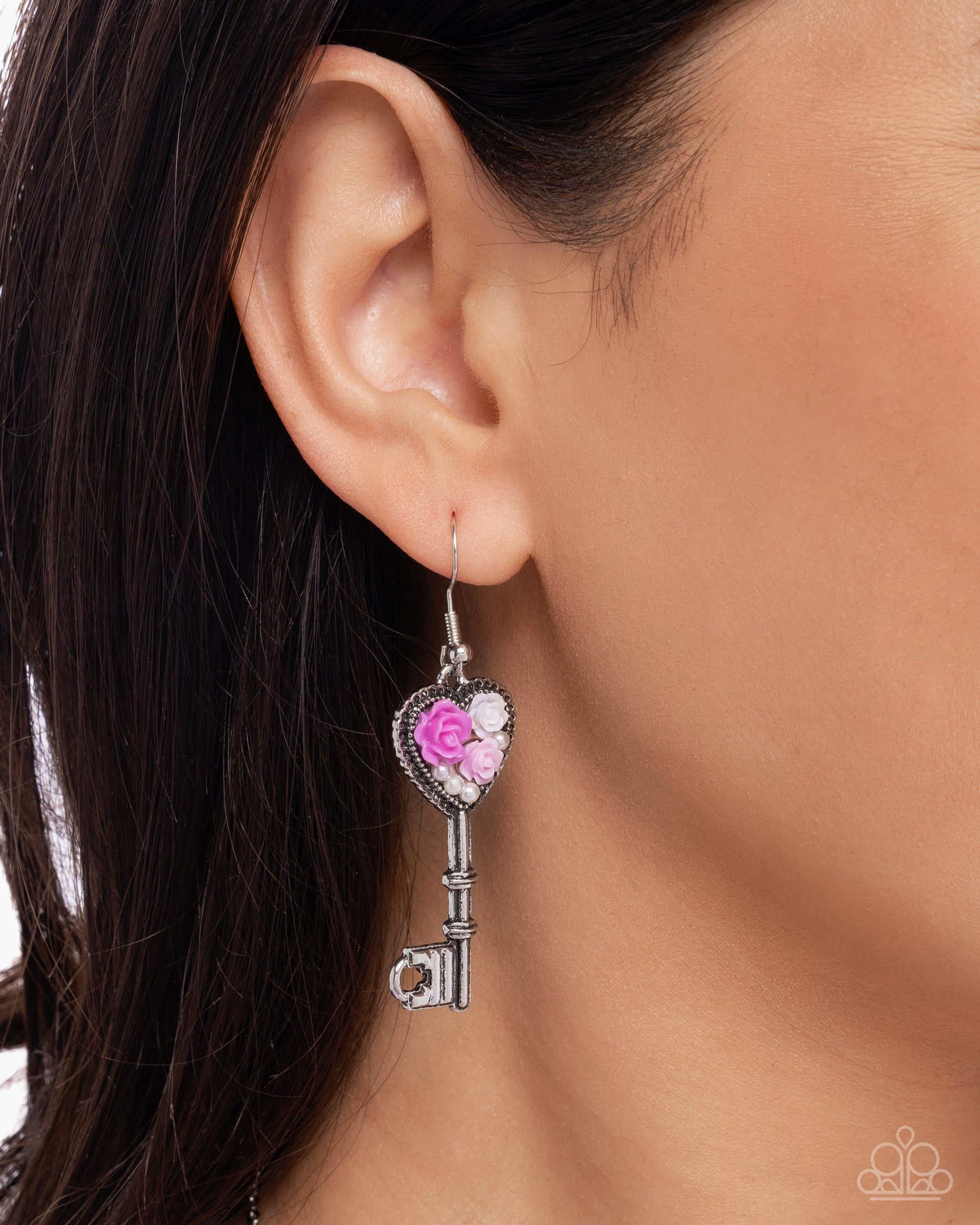 Silver key-shaped earring with pink gem worn by a person
