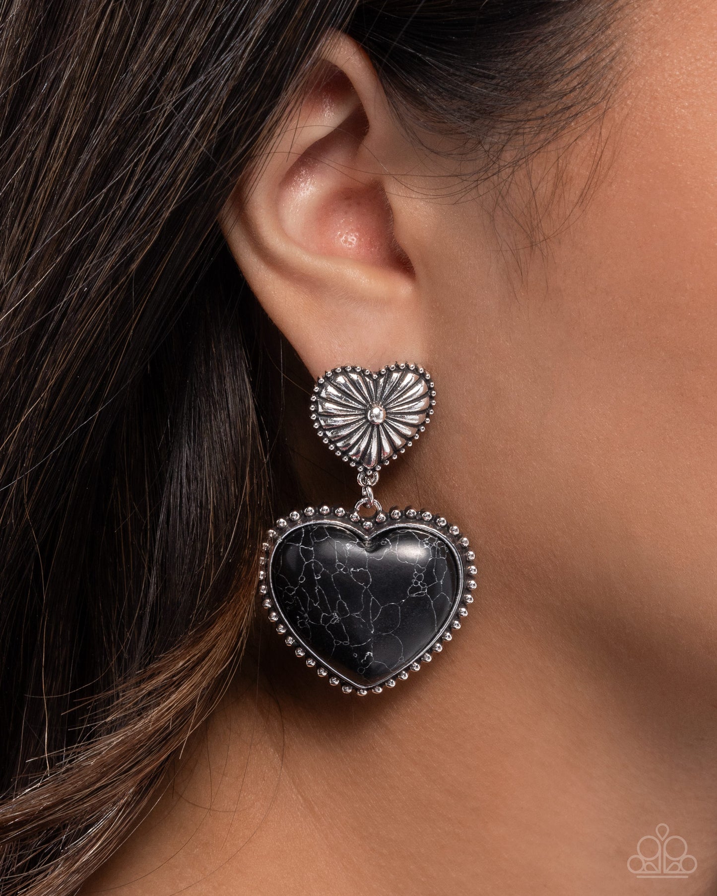 Heart-shaped earring with black stone and silver detailing worn by a person.