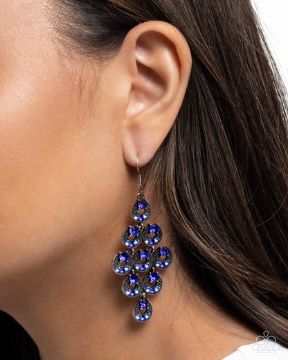 Close-up of a person wearing a blue teardrop earring with a blurred background