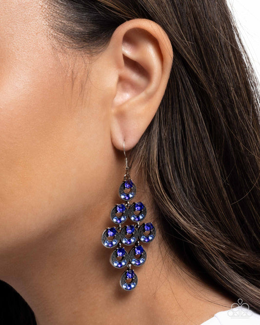 Close-up of a person wearing a blue teardrop earring with a blurred background