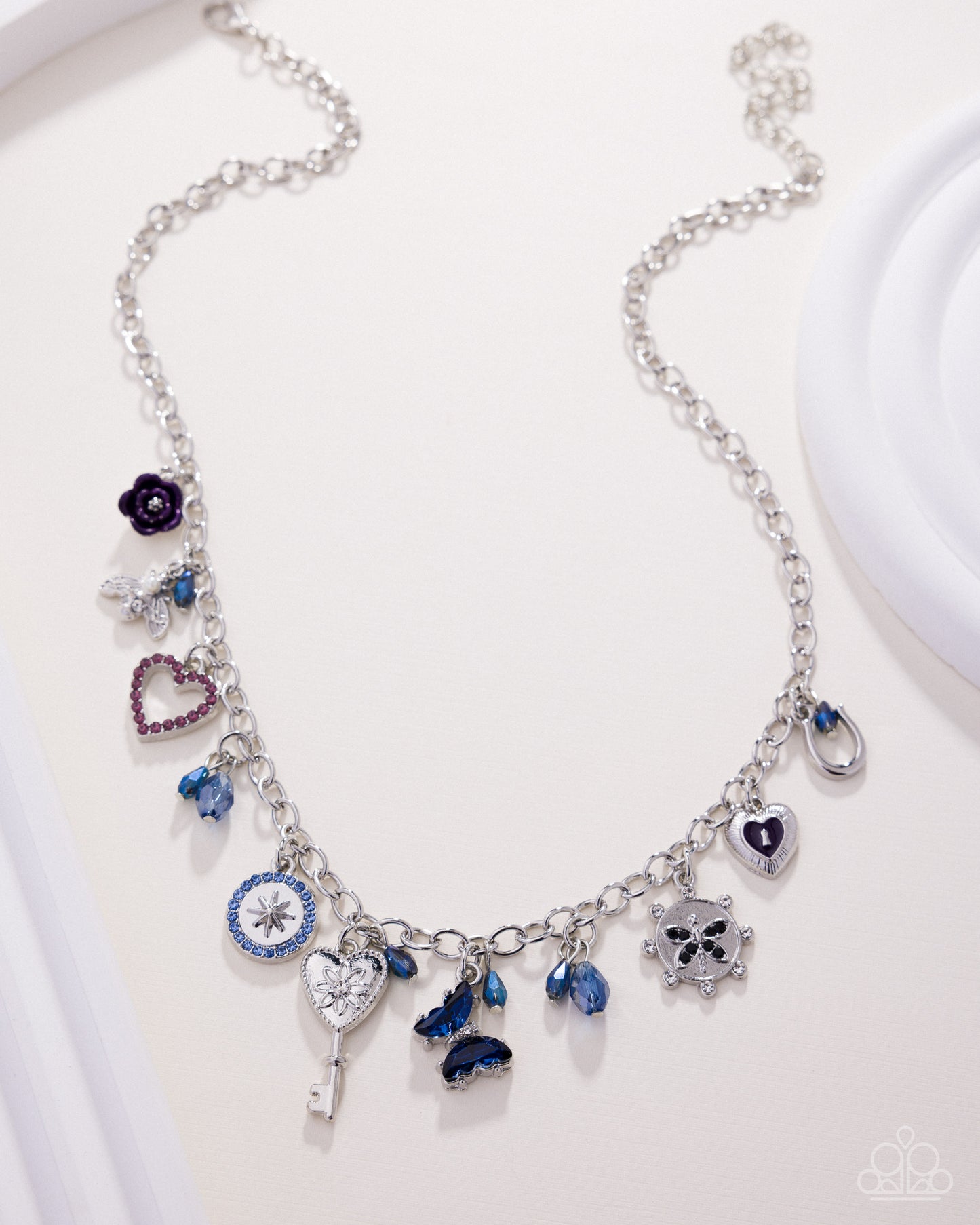 Silver necklace with various charms on a white background
