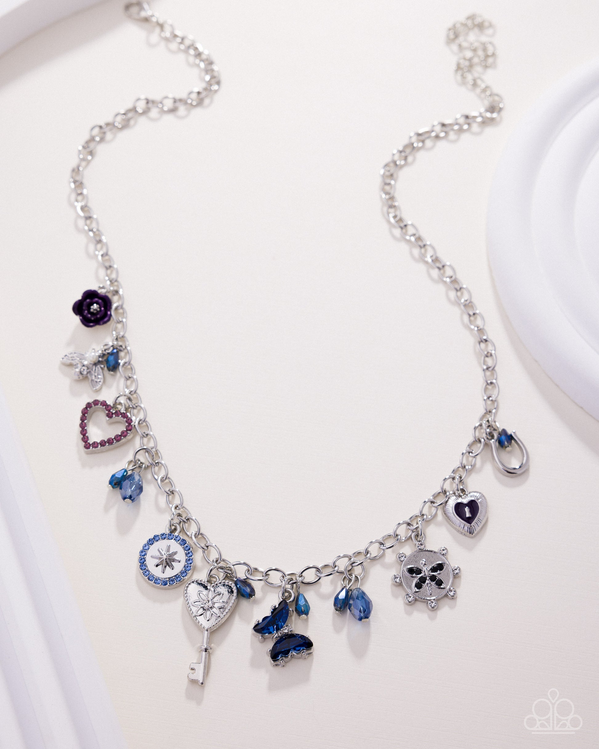 Silver necklace with various charms on a white background