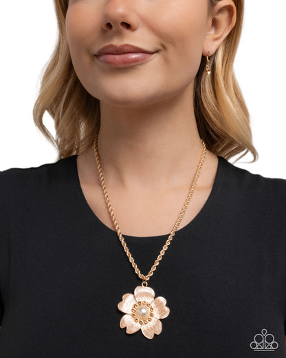 Woman wearing a gold flower pendant necklace on a plain background