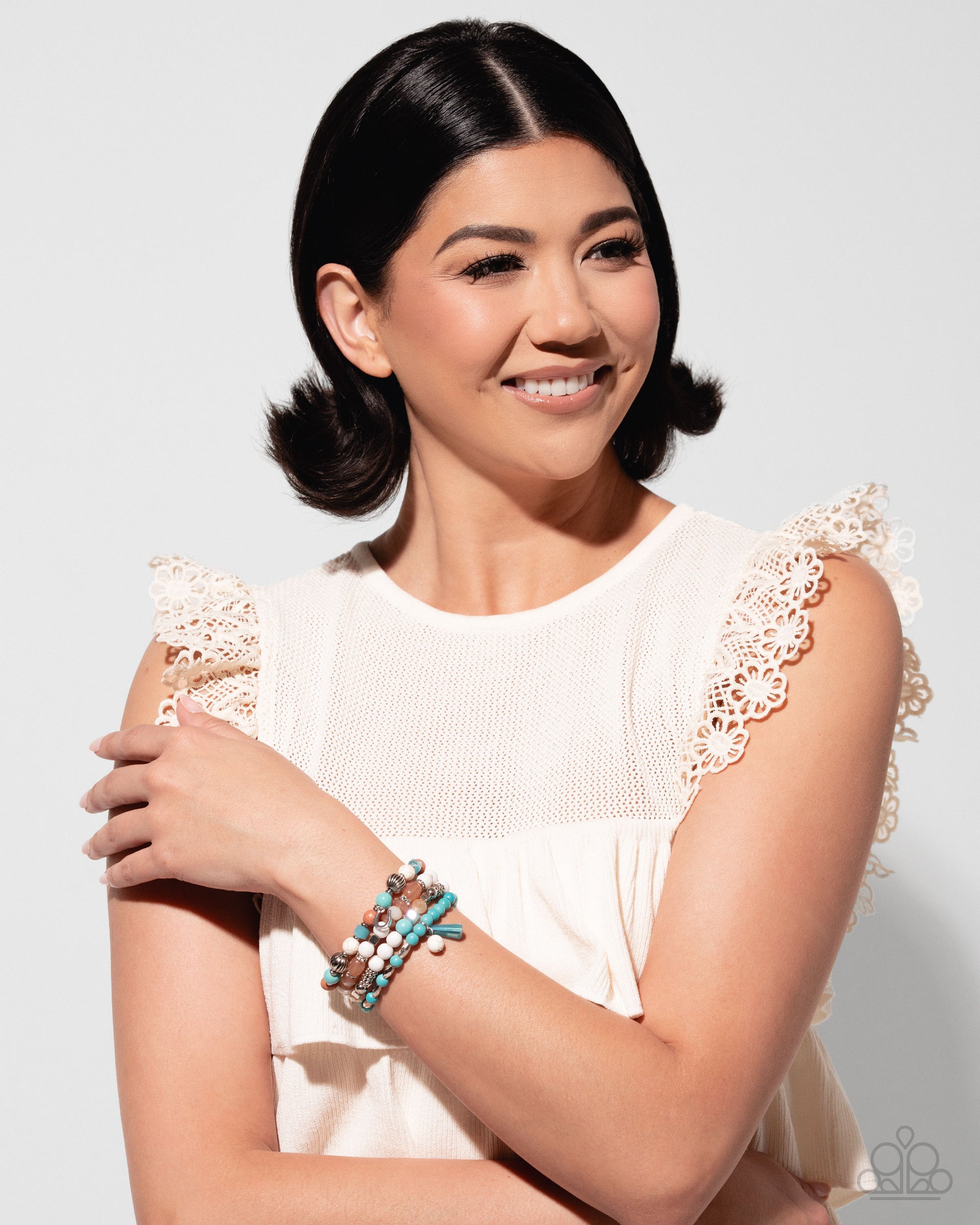 Woman wearing a white dress with lace details and multiple bracelets on a light gray background