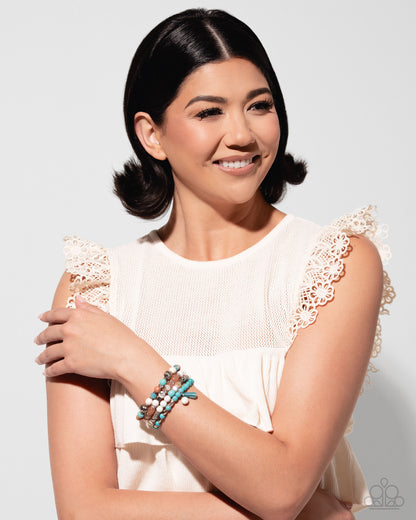 Woman wearing a white dress with lace details and multiple bracelets on a light gray background