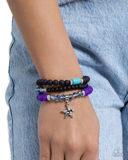 Hand wearing multiple beaded bracelets with a star charm against a denim background