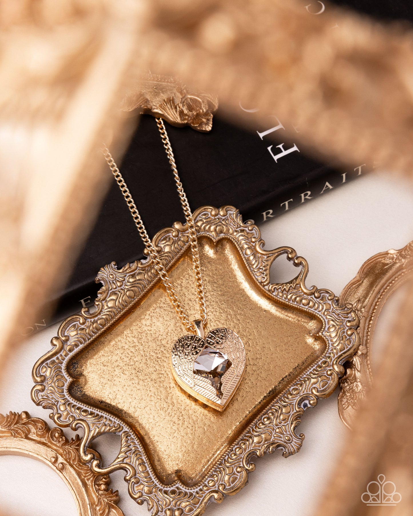 Gold heart-shaped necklace on an ornate gold display stand with blurred background