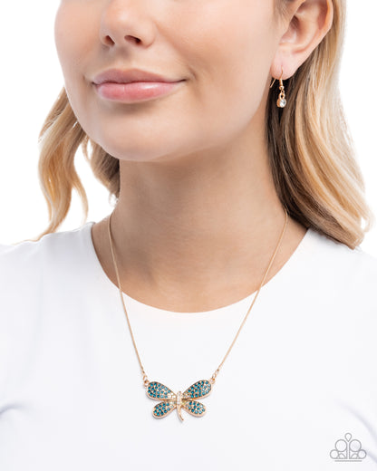 Close-up of a woman wearing a gold butterfly necklace with green gemstones on a white background