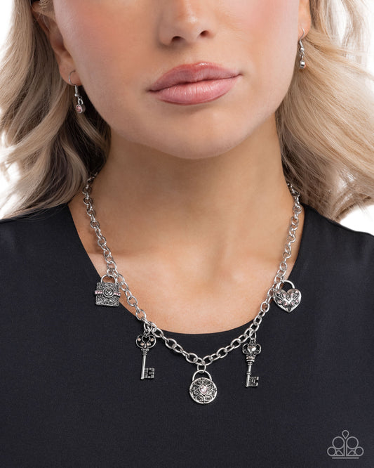 Necklace with key and heart charms worn by a person against a black background